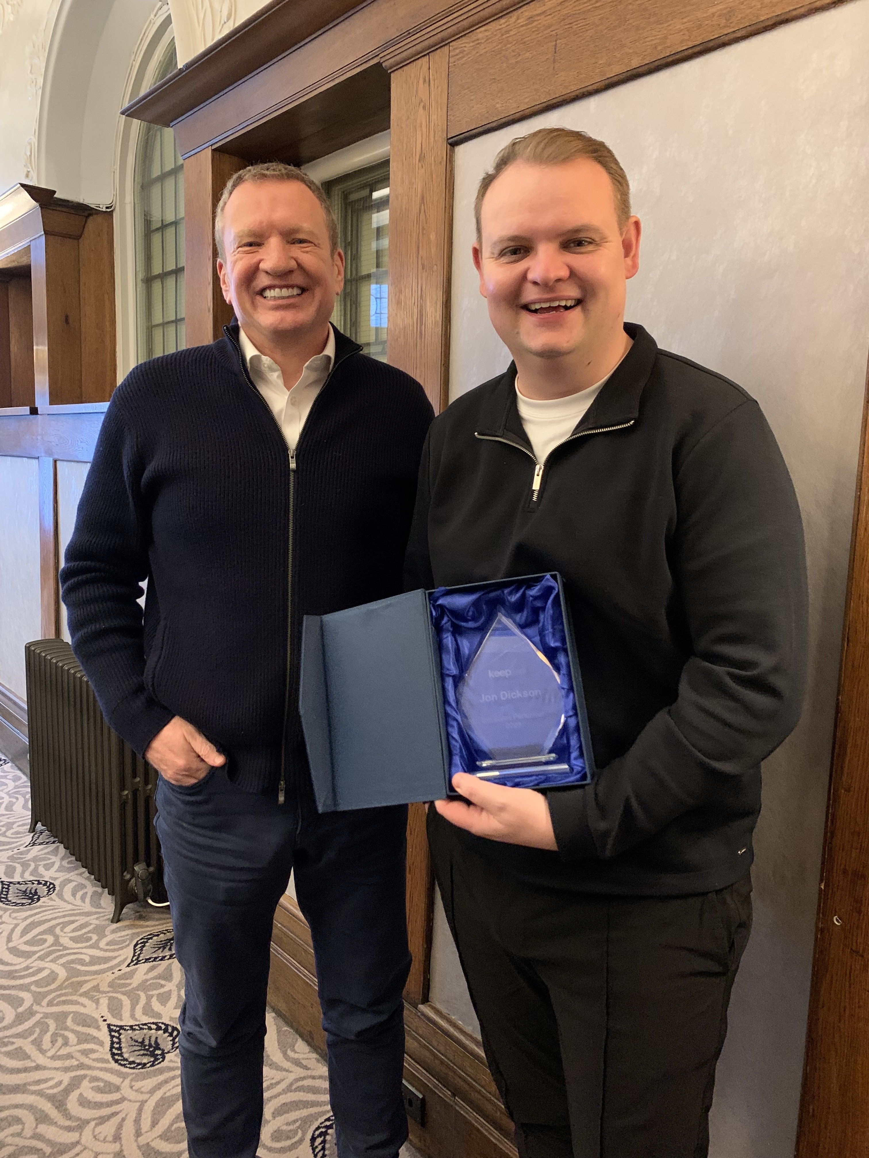 Two Keepme colleagues smiling together as one presents Jon Dickson with a glass award