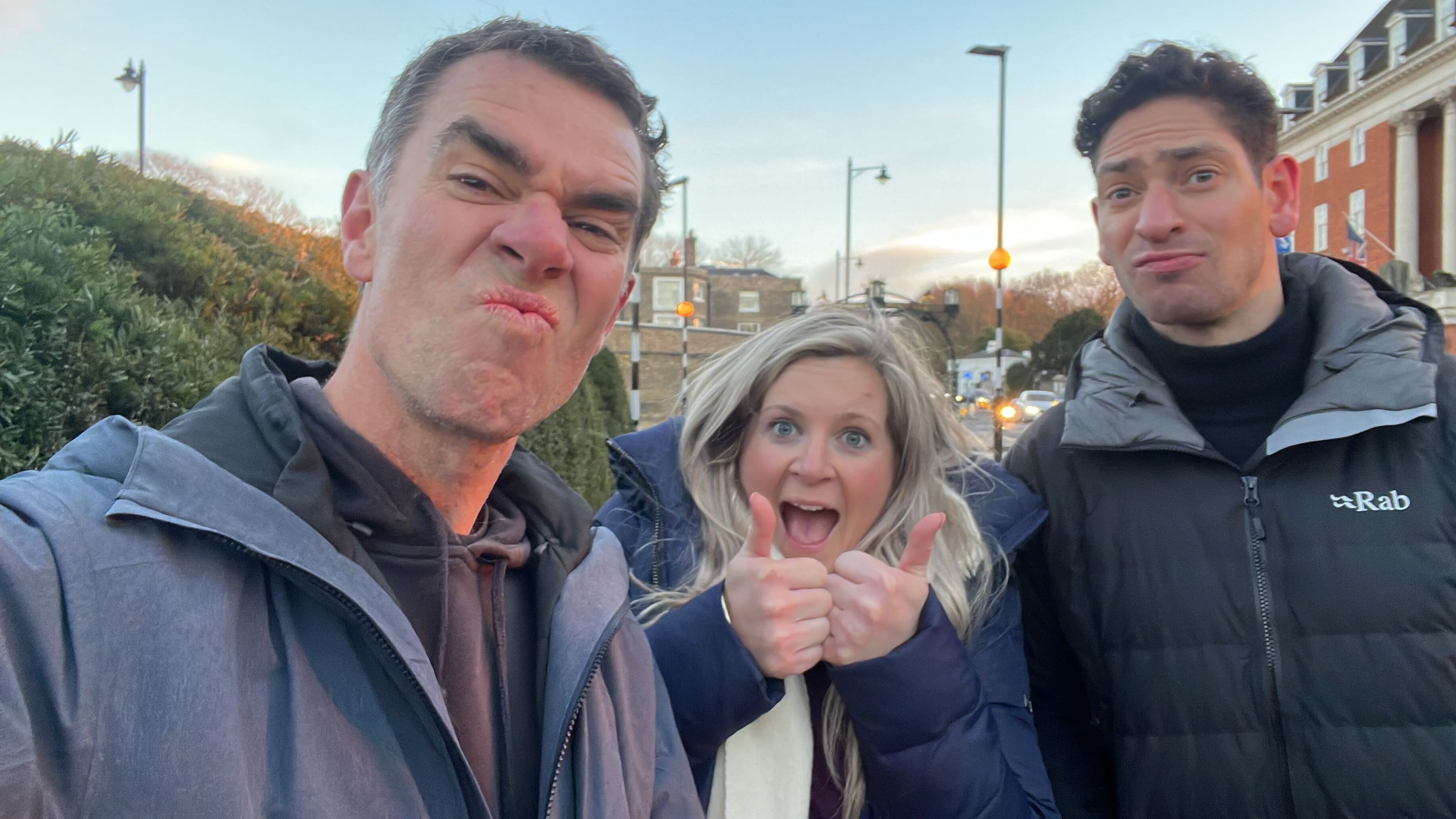 Three Keepme colleagues pulling playful faces and giving a thumbs up on a street at dusk